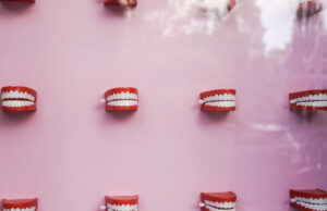 Red toy dentures with white teeth arranged on a pink background, symbolizing oral hygiene and dental care.