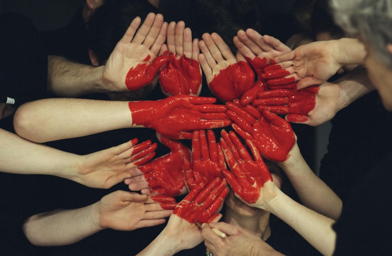 A group of hands painted with red hearts joining together, symbolizing unity, love, and the power of shared stories.