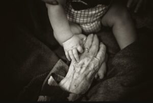 A black and white photograph capturing the gentle touch between a newbornâ€™s tiny hand and an elderly personâ€™s wrinkled hand, symbolizing the cycle of life, love, and generational connection.